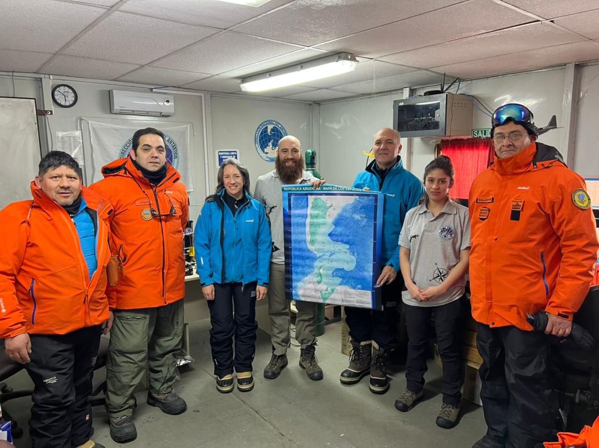 Guillermo Carmona, sosteniendo el mapa del territorio argentino, posa en la Base Marambio junto a la Directora Nacional del Antártico (DNA), Patricia Ortúzar y otros integrantes de la misión.