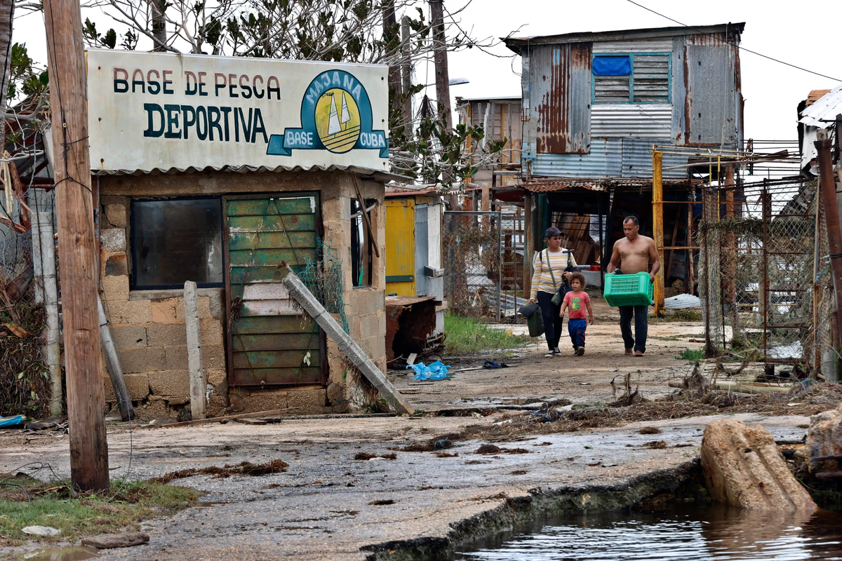 Una familia camina con sus pertenencias por una calle afectada tras el paso del huracán Rafael, en Playa Majana, en la provincia de Artemisa, Cuba. Crédito: EFE. Una familia camina con sus pertenencias por una calle afectada tras el paso del huracán Rafael, en Playa Majana, en la provincia de Artemisa, Cuba. Crédito: EFE.