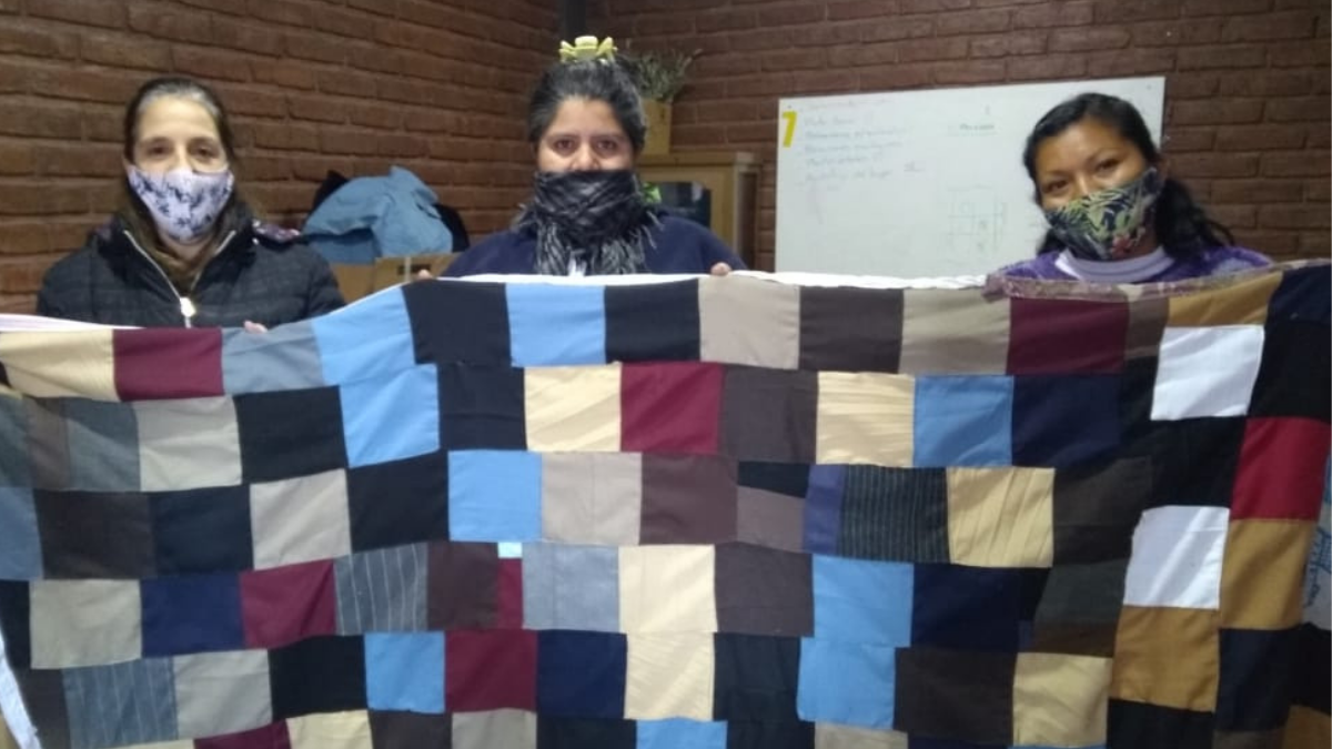 Carina -primera de derecha a izquierda- y sus compañeras: Yolanda (centro) y Claudia (primera de izquierda a derecha). Las mujeres muestran una de las mantas confeccionadas en el taller