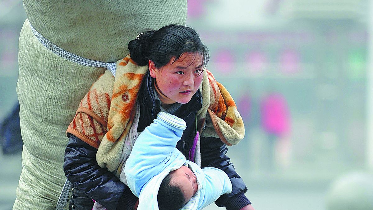 Bamuyubumu, que entonces tenía 21 años, sostiene a un bebé en un brazo y lleva un gran saco en la espalda mientras se apresura a tomar un tren en la estación de Nanchang, provincia de Jiangxi, en enero de 2010. ZHOU KE / XINHUA &nbsp;