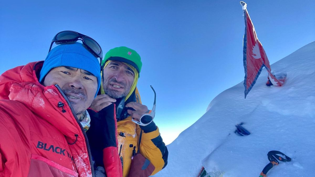 Ulises Corvalán posa junto a un integrante de la expedición al ochomil, junto a una bandera de Nepal.