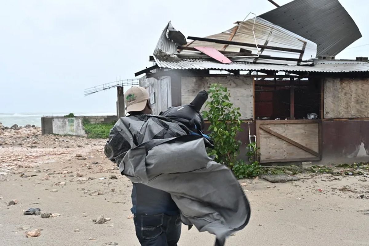 Un hombre carga una lona para cubrir el techo de una casa antes del paso del huracán Melissa este lunes, en la playa pesquera de Hellshire, en Portmore en Jamaica. Crédito: EFE/Rudolph Brown.
