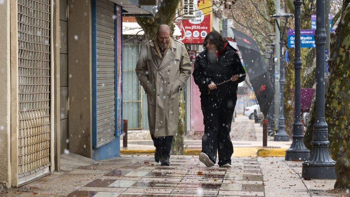 Un hombre y una mujer caminan por Godoy Cruz bajo la nieve. Un hombre y una mujer caminan por Godoy Cruz bajo la nieve.