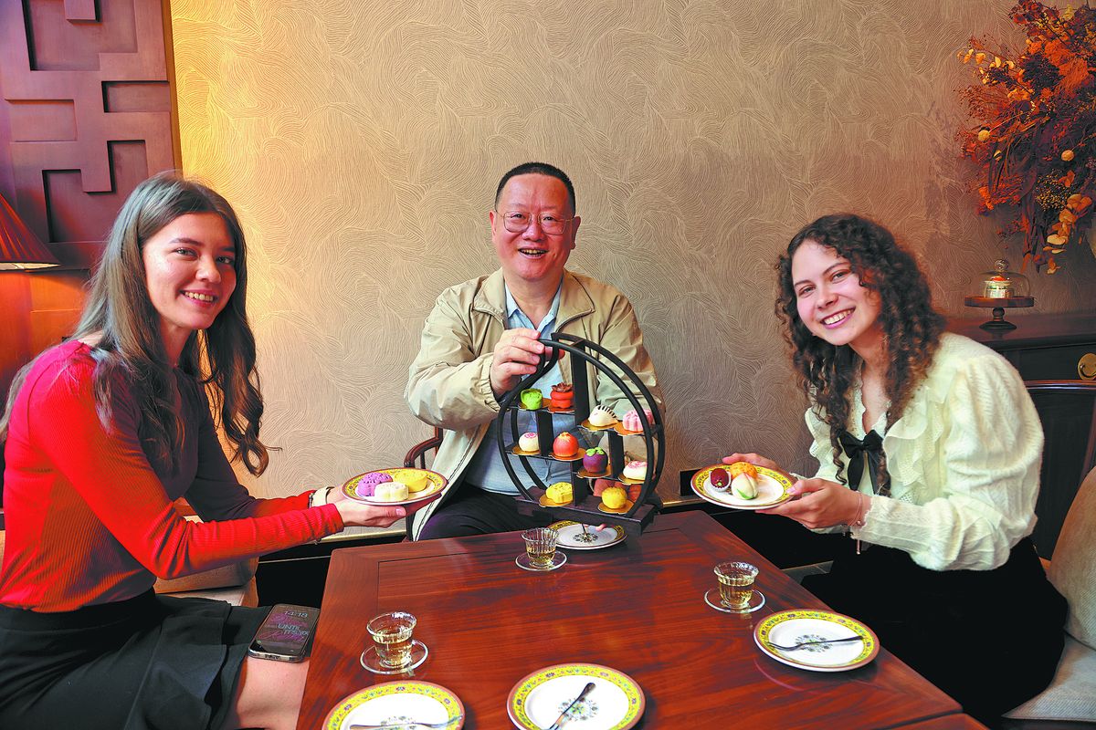 Cheng Sheng (centro), director de recomendaciones culinarias de la campa&ntilde;a 240 horas de paseo gastron&oacute;mico por Beijing, y dos invitadas extranjeras prueban reposter&iacute;a tradicional china. PARA USO DE CHINA DAILY.