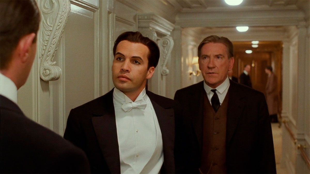 David Warner, interpretando Spicer Lovejoy, a las espaldas de Cal Nathan (Billy Zane) en Titanic.