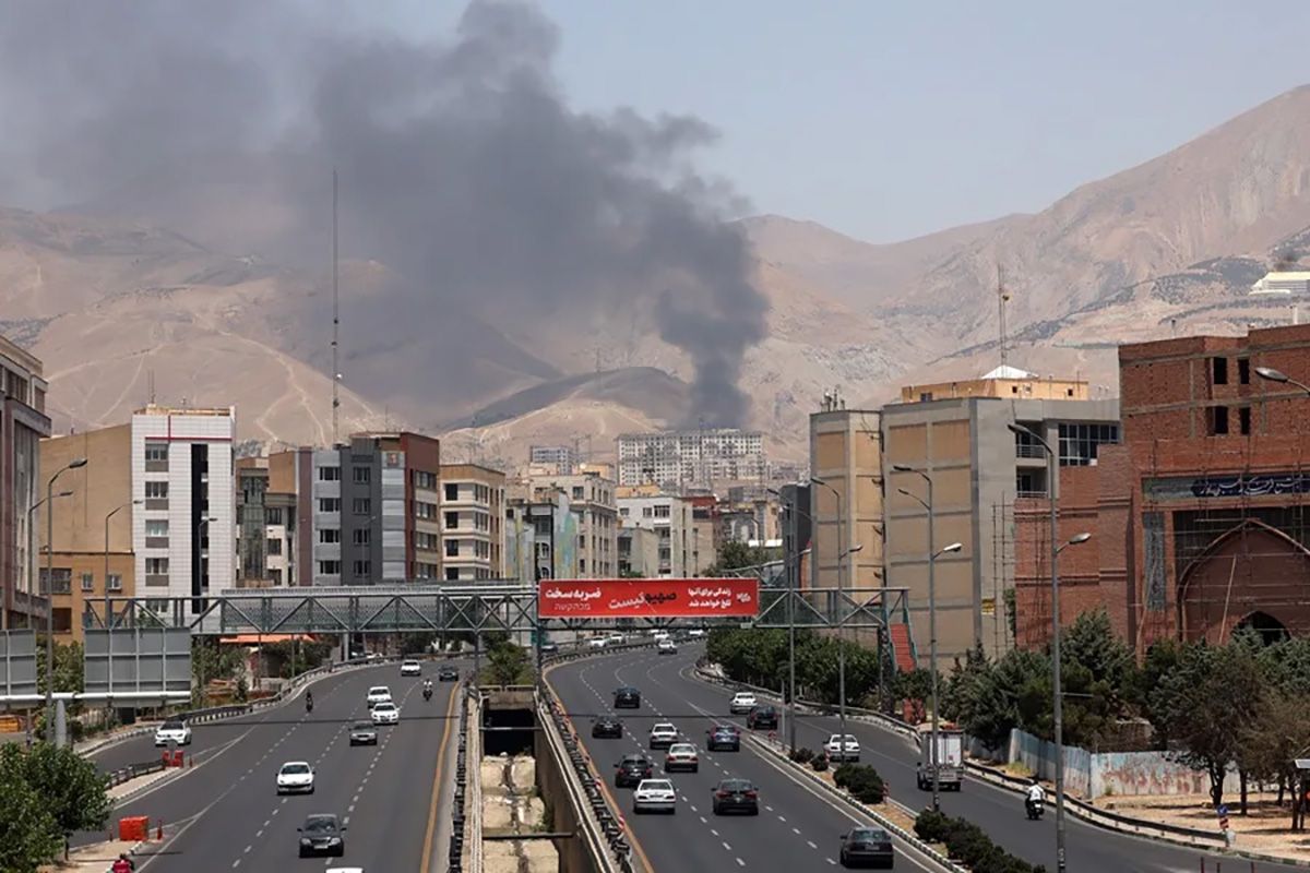 Vehículos circulando por una autopista mientras al fondo sale humo de una refinería de petróleo