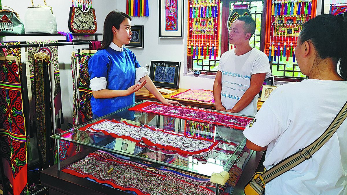 Xu (izquierda) habla sobre la producción de bordados miao en una tienda local. PARA USO DE CHINA DAILY 