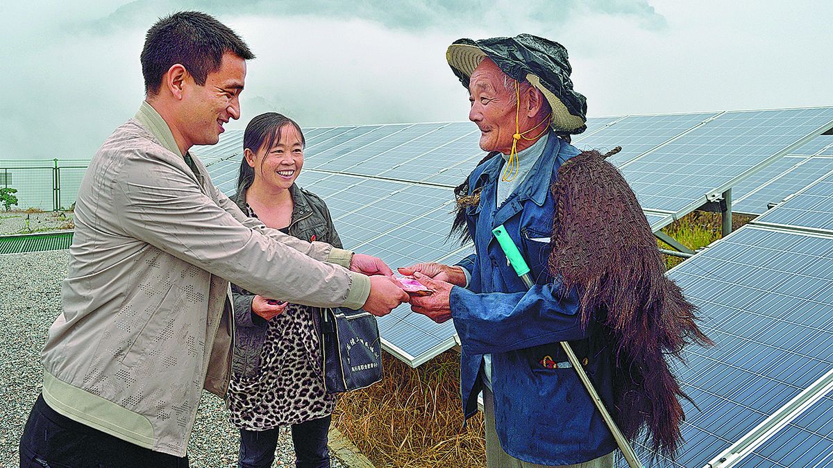 Un aldeano recibe su pago por limpiar paneles fotovoltaicos de la mano de un funcionario local. LEI YONG / PARA CHINA DAILY