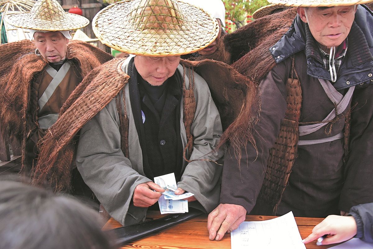 Los trabajadores temporales reciben su salario diario después de sus turnos de interpretar al legendario personaje histórico Jiang Ziya en una zona escénica de la provincia de Hunan. PARA USO DE CHINA DAILY